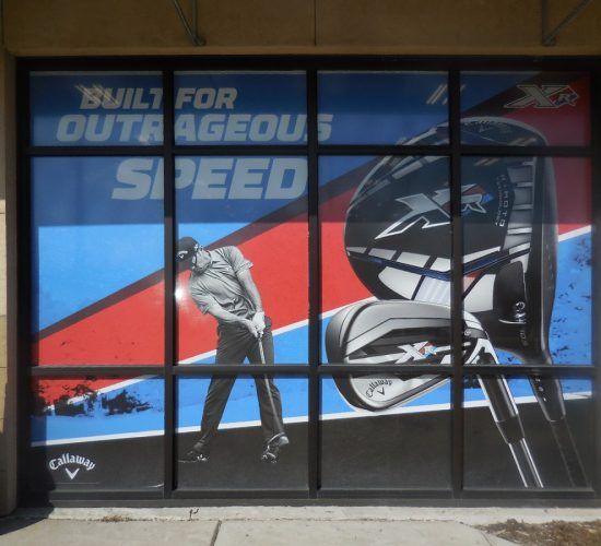 Window display advertising Callaway golf clubs. Golfer swinging club, clubs in the background, blue, red, and black color scheme.