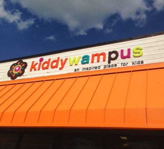 Kiddy Wampus sign on a building with orange awning; blue sky with clouds.