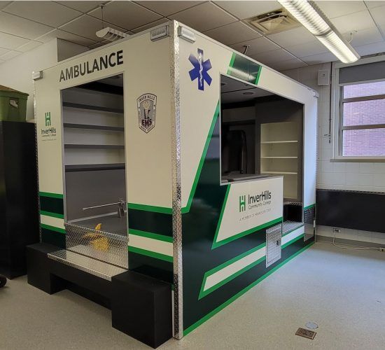 Ambulance simulator with green and white accents, used for training. Interior features shelves and medical equipment spaces.
