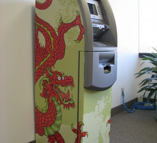 ATM with a red dragon design on its side, located indoors near a plant and wall.