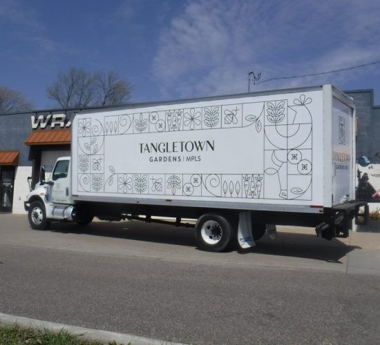 White Tangle Town Gardens truck parked in front of a building. Floral design and logo on the side.