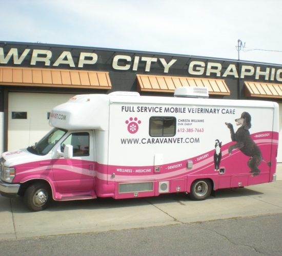 Pink and white Caravan Vet mobile clinic; black poodle graphic, parked outside a building.
