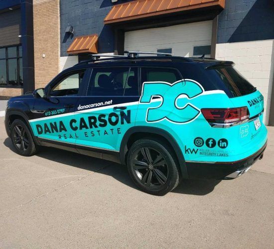 Black SUV with teal Dana Carson Real Estate branding, parked in front of a building.