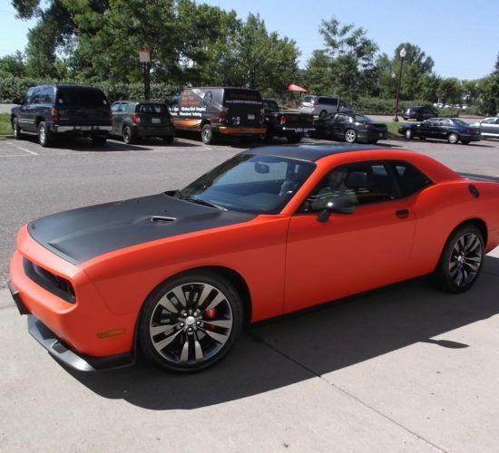 Orange Dodge Challenger with black hood and roof parked in a lot.