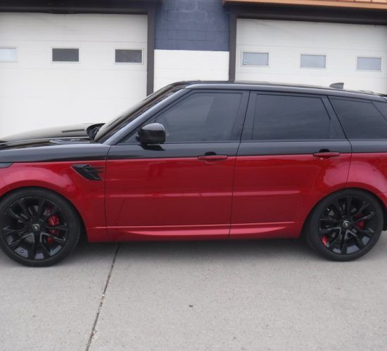 Red and black Range Rover parked in front of garage doors, with black wheels and tinted windows.