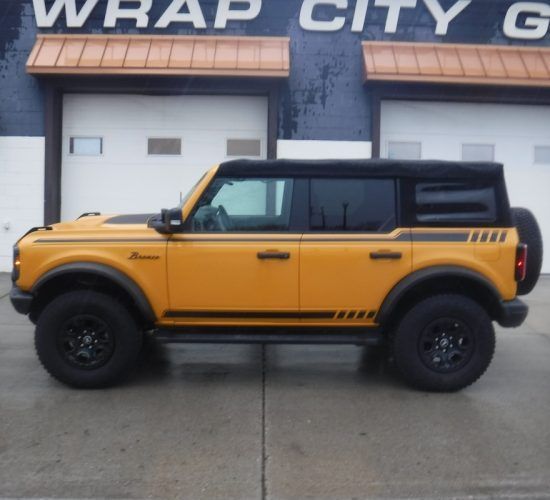 Yellow Ford Bronco with black accents parked in front of a building with garage doors.