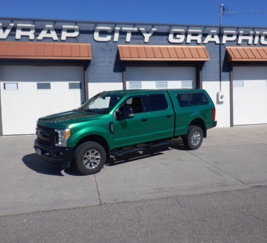 Green truck with matching camper shell parked in front of Wrap City Graphics building.