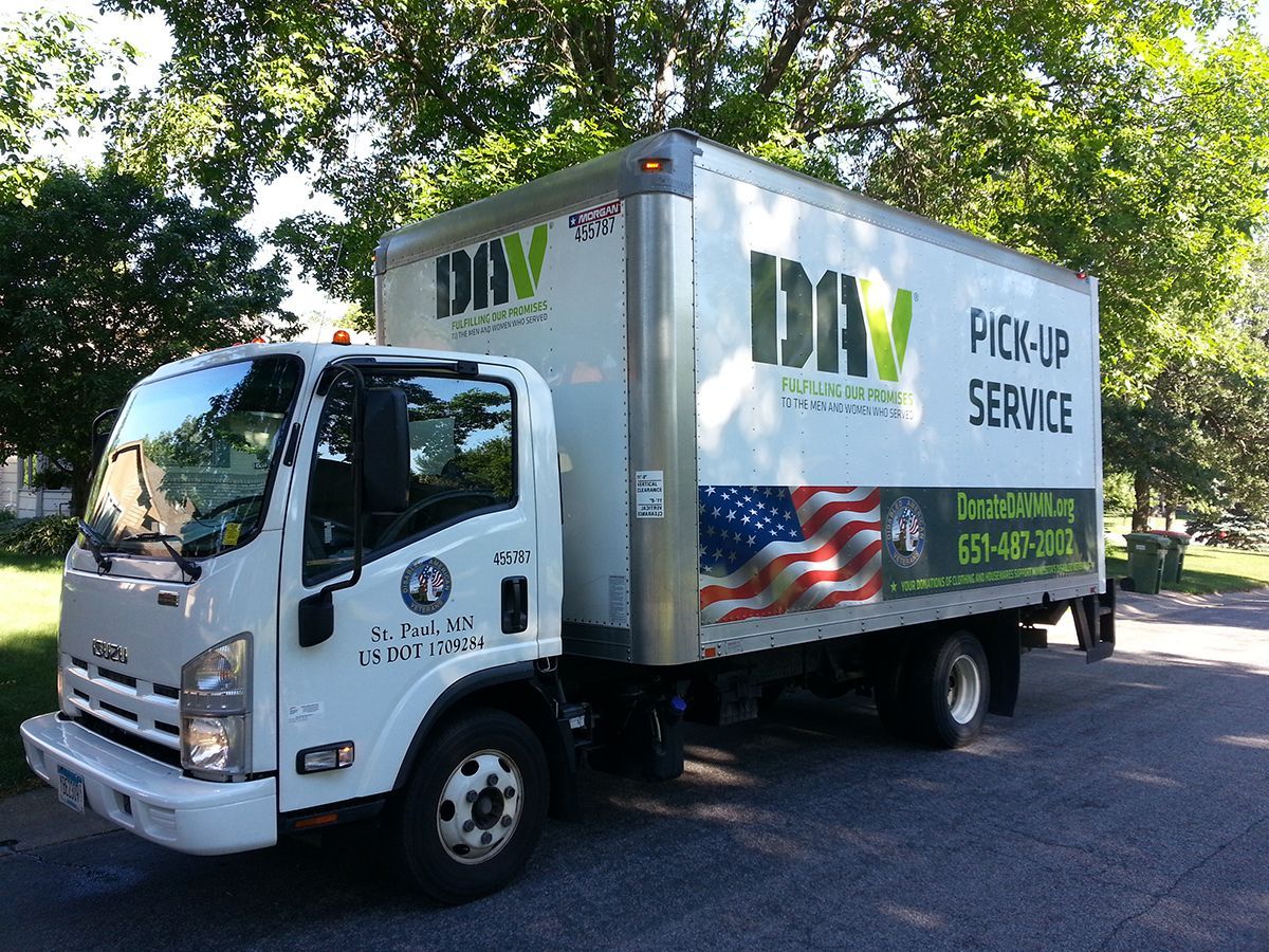 White DAV truck with pick-up service, parked on a street with a US flag graphic.