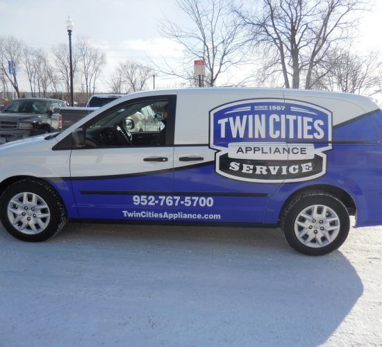 White and blue Twin Cities Appliance Service van parked on snow.