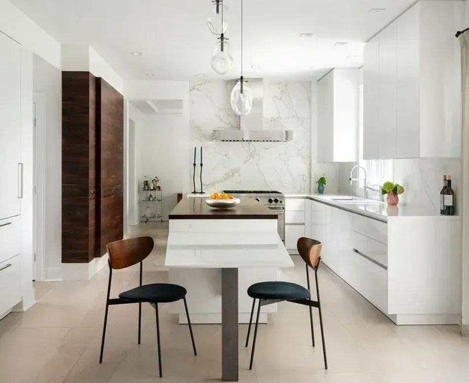 Modern white kitchen with marble backsplash, dark wood island, two chairs, and pendant lights.