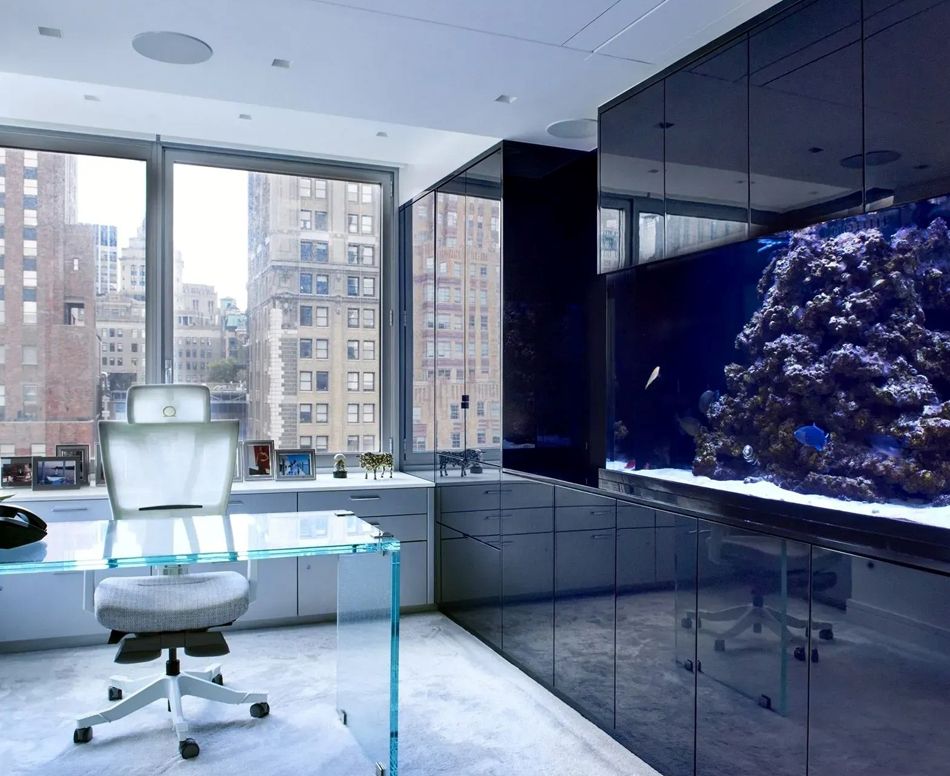 Modern office with glass desk, city view, and large aquarium on wall.