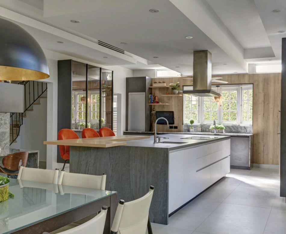 Modern kitchen with island, dining area, and stairs. Gray, white, and wood tones; orange chairs.