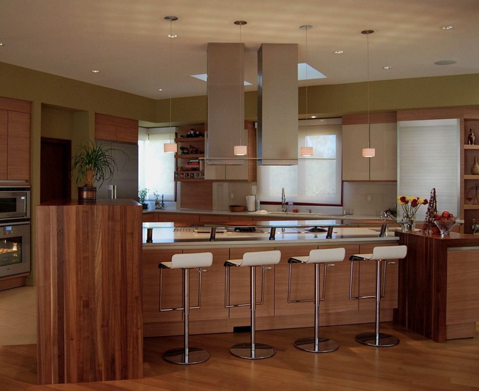 Modern kitchen with light wood cabinets, island with stools, stainless steel appliances, and pendant lights.