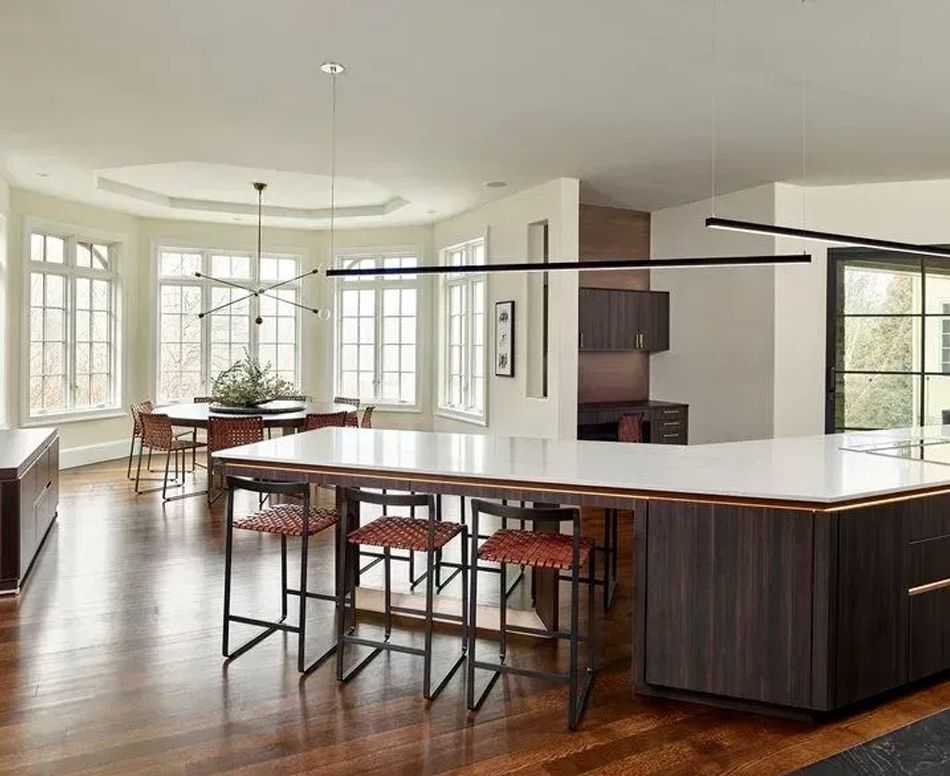 Modern kitchen with dark wood island, seating, and dining area with large windows.