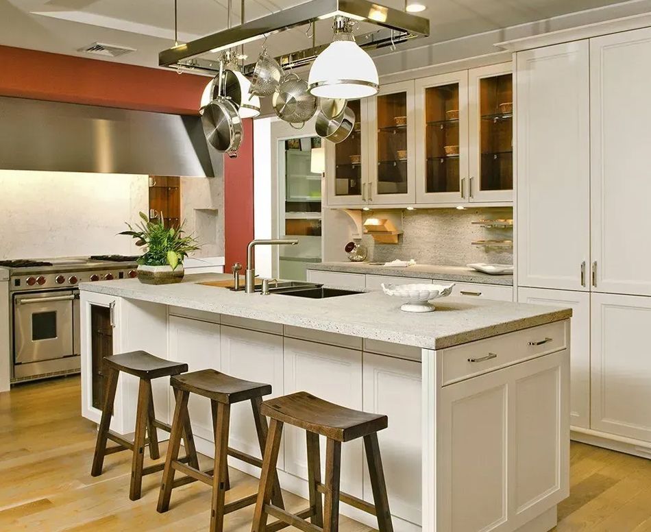 Modern white kitchen with island, stools, stainless steel appliances, and cookware rack.