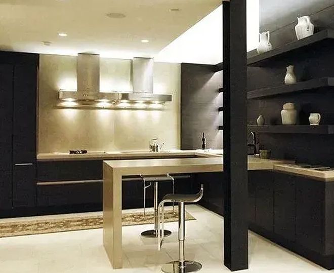 Modern kitchen with dark cabinets, stainless steel island with stools, and open shelves with decorative items.