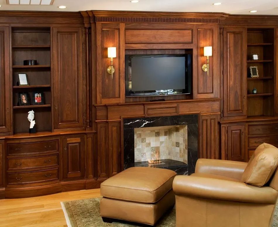 Wooden built-in entertainment center with TV, fireplace, bookshelves, sconces, and leather chair with ottoman.