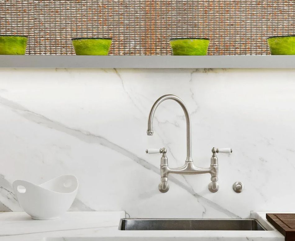 Stainless steel kitchen sink and faucet against a white marble backsplash, with a shelf holding green pots.
