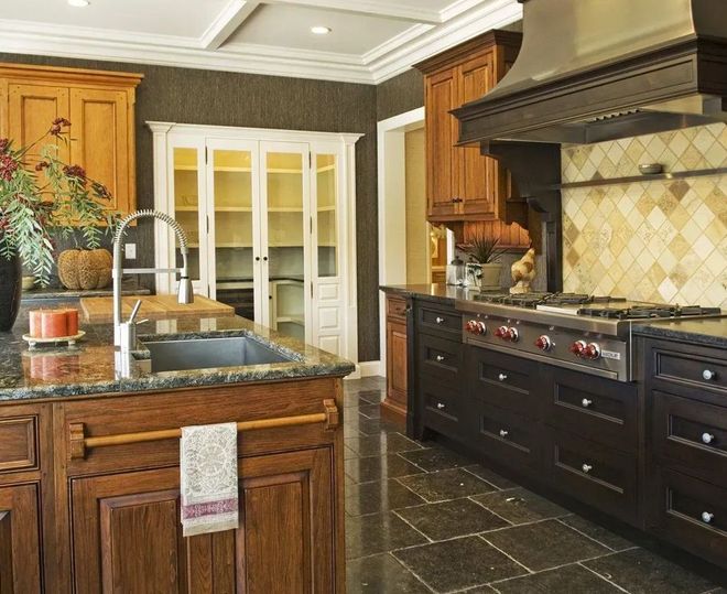 Luxurious kitchen with dark wood cabinets, granite countertops, and stone floor.