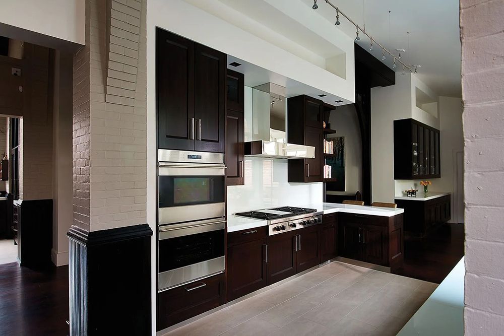 Dark wood kitchen with stainless steel appliances, white countertops, and white backsplash.