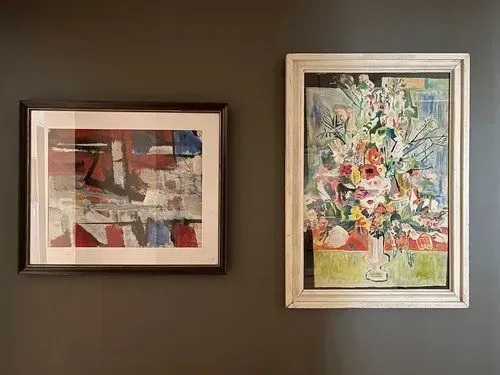 Two framed artworks on a dark gray wall: an abstract composition with red and blue, and a floral still life.