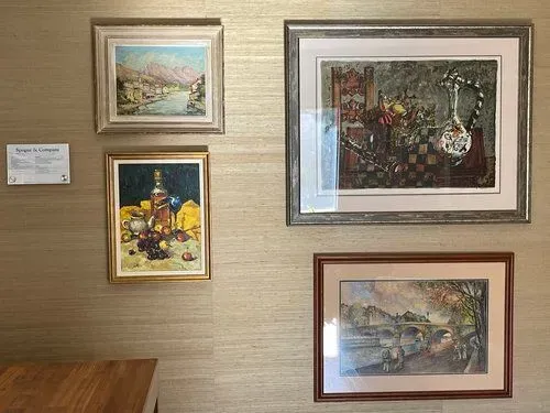 Four framed paintings on a textured wall, depicting landscapes and still life. A small plaque is beside the top left painting.
