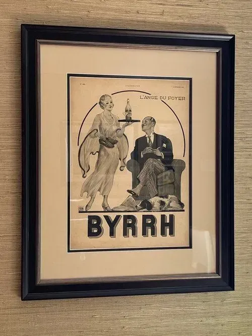 Vintage BYRRH advertisement, framed. A server offers a bottle to a man seated in an armchair with a dog.