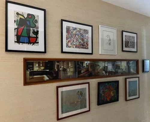 A wall displays framed art and a long mirror, arranged in a row on textured, light-colored wallpaper.