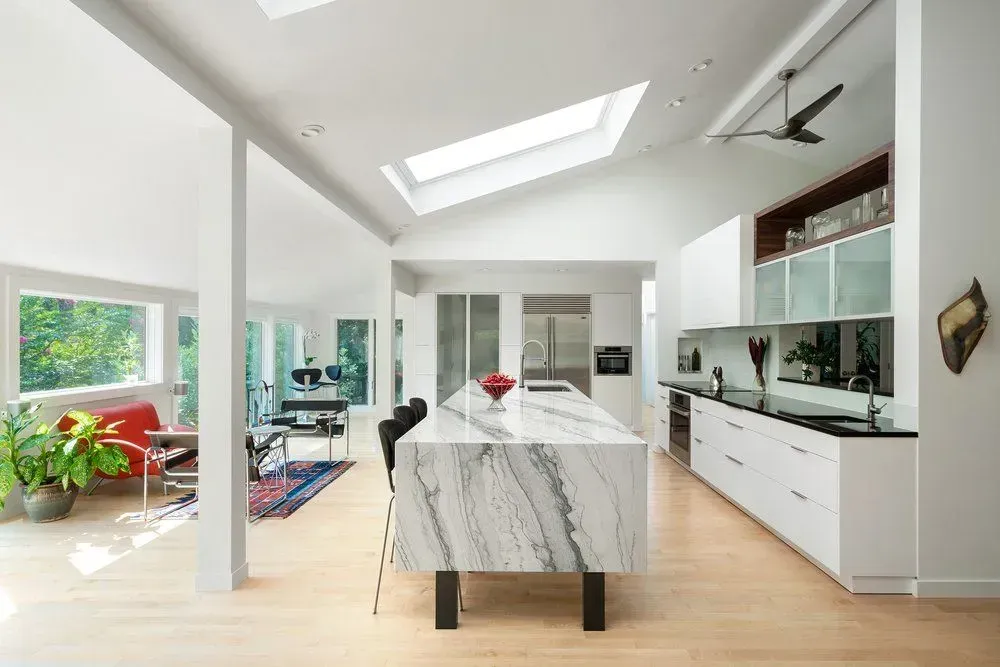 Modern kitchen with white cabinets, marble island, and skylights.