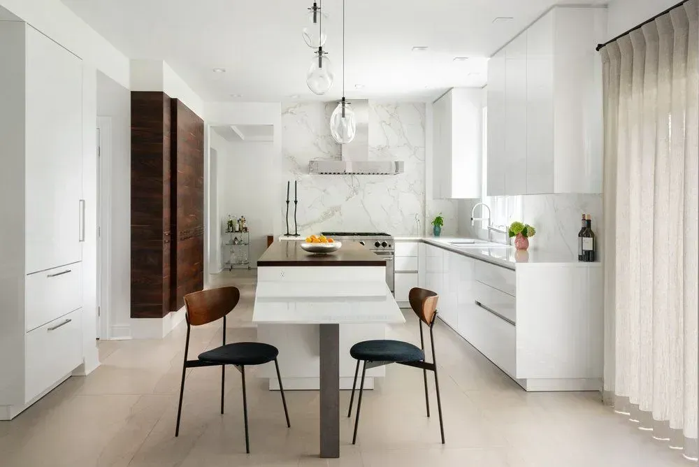 Modern white kitchen with island, marble backsplash, and wooden accents.