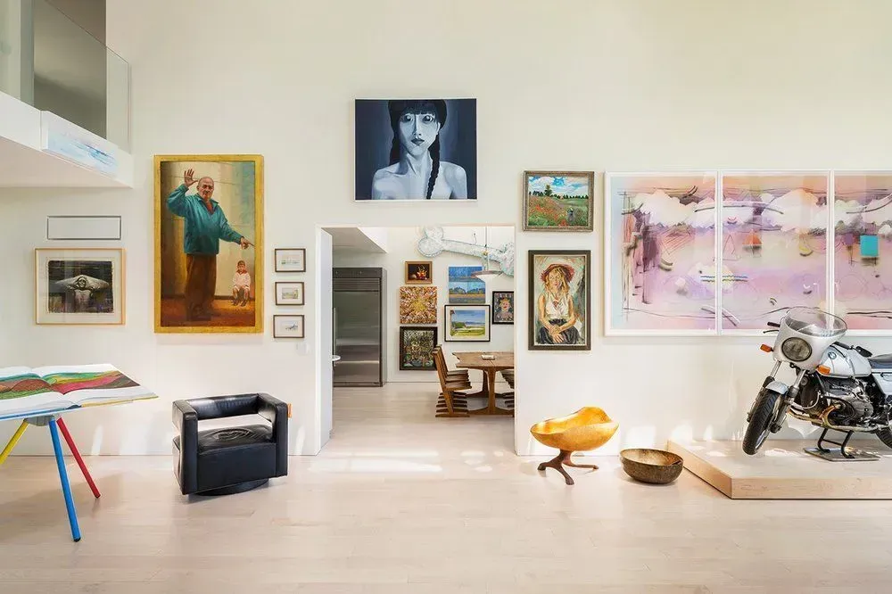 A bright, airy room with various artwork on the walls and a motorcycle on a display platform.