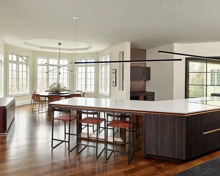 Modern kitchen with island, seating, dark wood cabinetry, and large windows.