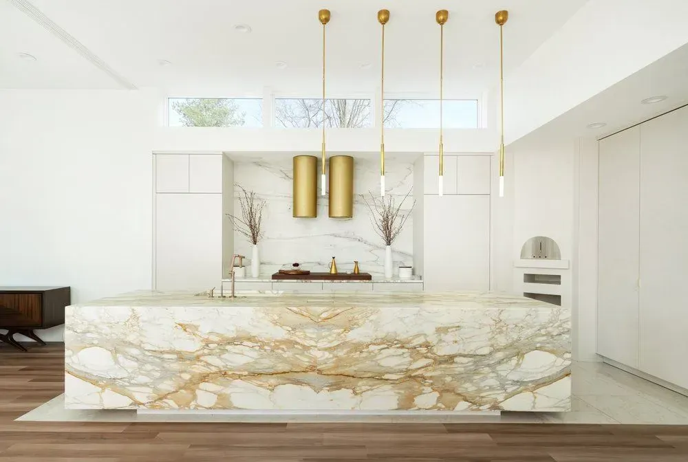 Modern kitchen with marble island, gold pendant lights, white cabinets, and wooden floors.