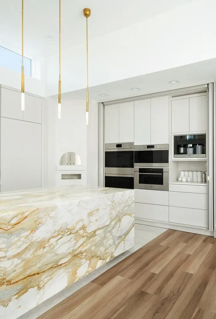 Modern kitchen with marble island, gold pendant lights, and built-in white cabinetry, and stainless steel appliances.