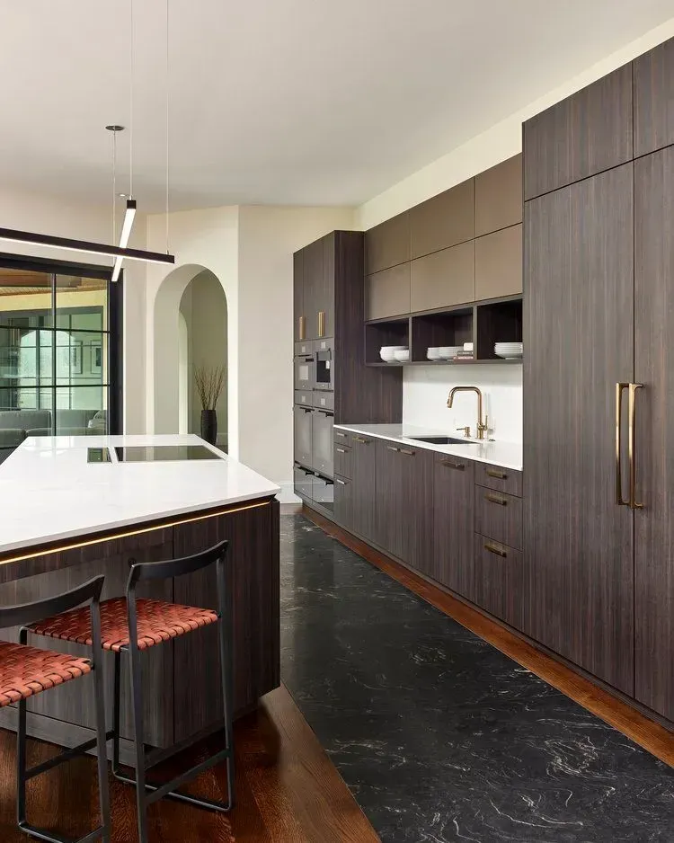 Modern kitchen with dark wood cabinetry, white countertops, and black marble floors.