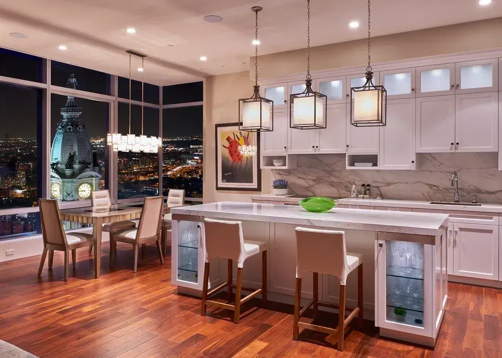 Modern kitchen with a city view at night, hardwood floor, white cabinets, and island with bar stools.