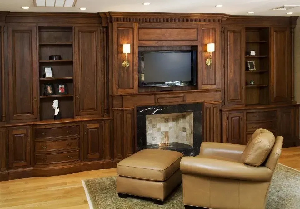Dark wood entertainment center with fireplace, TV, and armchair with ottoman.