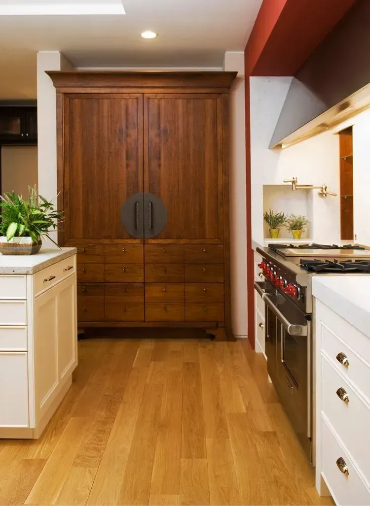 Wooden cabinet in a kitchen with white cabinets, stainless steel appliances, and wood flooring.