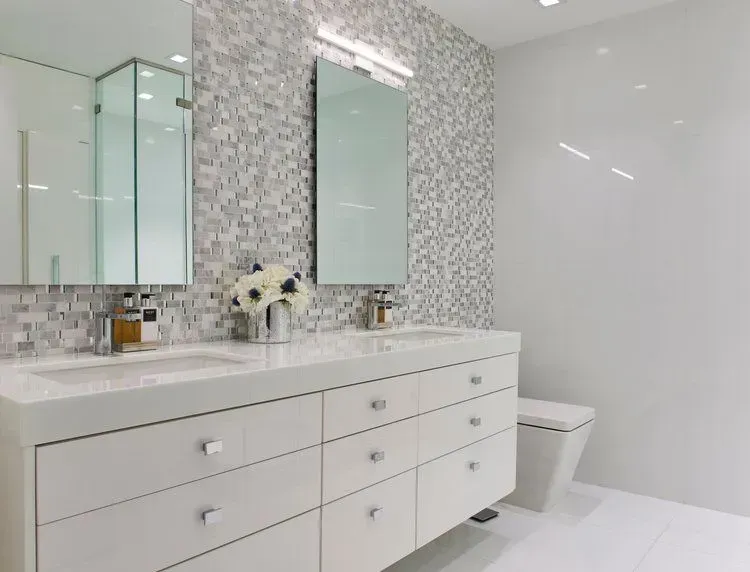 Modern white bathroom with double sink vanity, mosaic tile accent wall, and toilet.