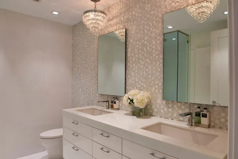 Modern bathroom with white vanity, two sinks, mirrors, and crystal chandeliers.