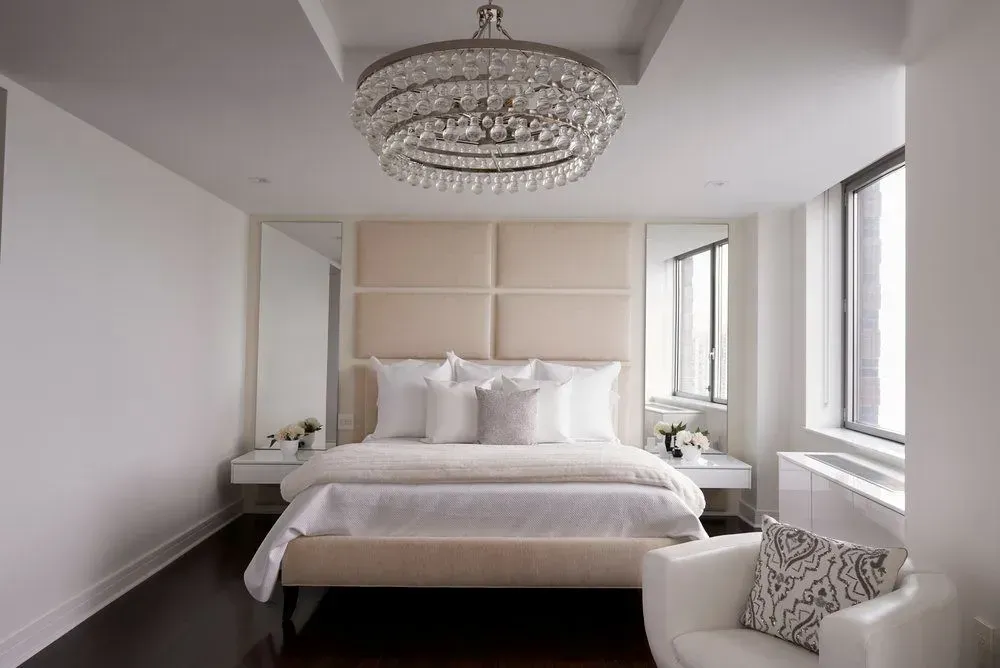 Luxurious bedroom with cream upholstered headboard, chandelier, and white furniture.
