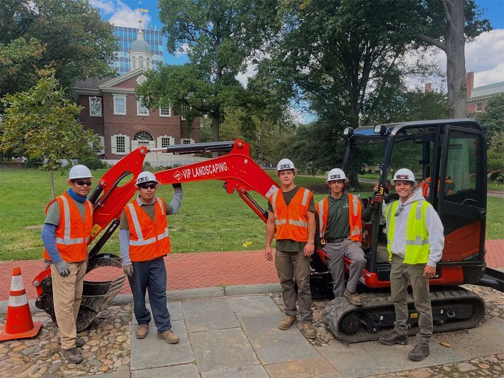 A group of construction workers are standing next to a small excavator.