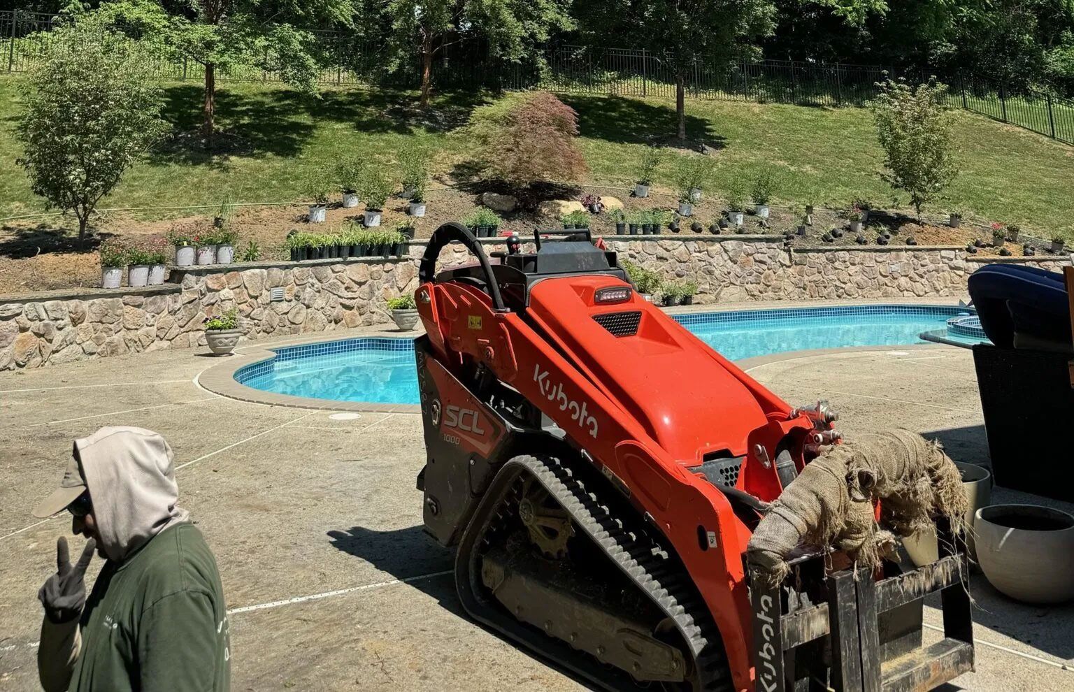 A man is standing next to a red tractor in front of a pool.