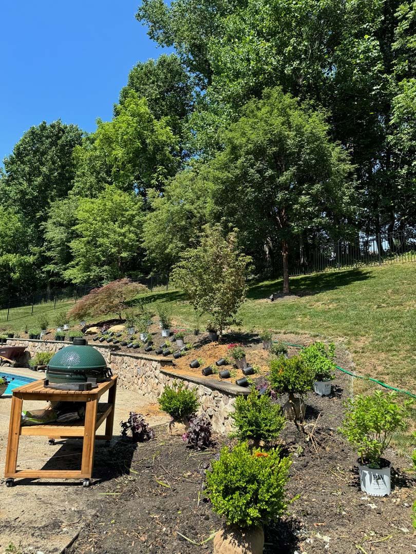 A large green egg grill is sitting on top of a wooden table in a backyard surrounded by trees.