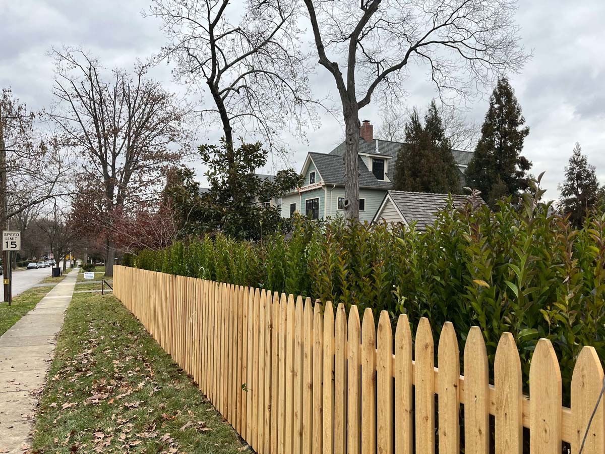 A wooden picket fence along a sidewalk in front of a house.