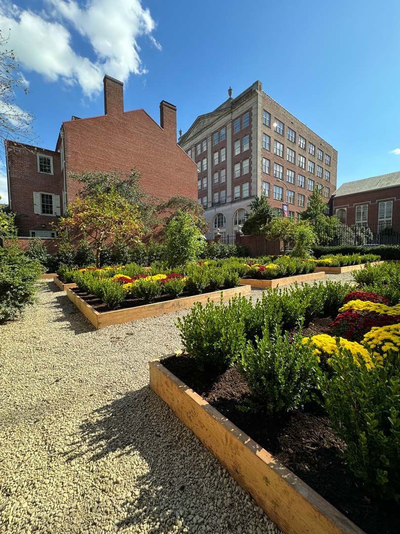 A garden with a brick building in the background and flowers in the foreground.