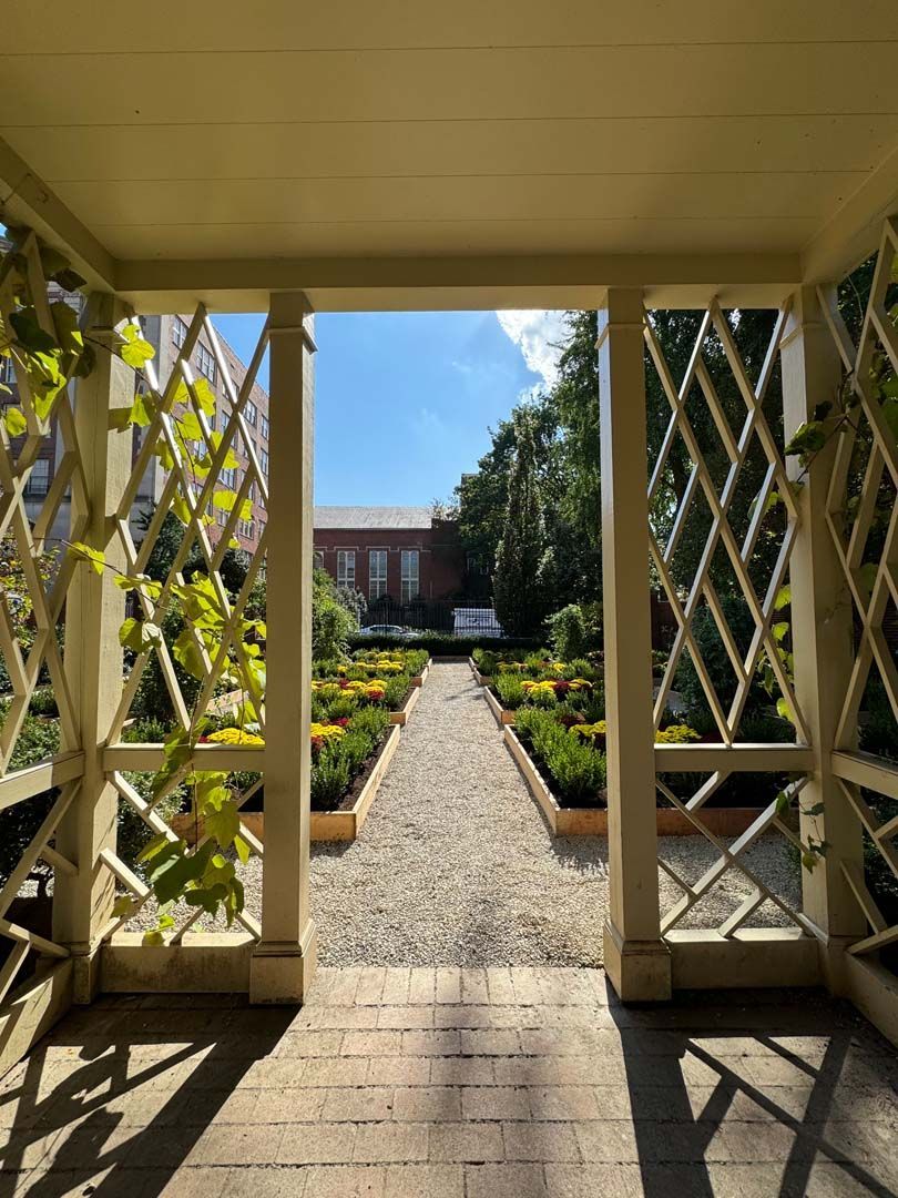 A view of a garden from a porch with a building in the background.
