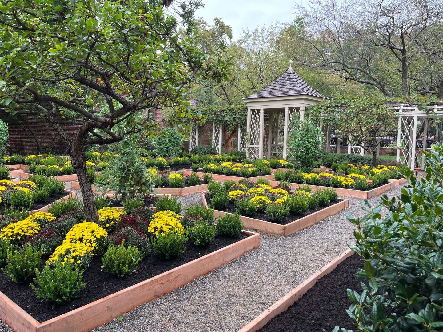 A garden with lots of flowers and trees and a gazebo in the background.