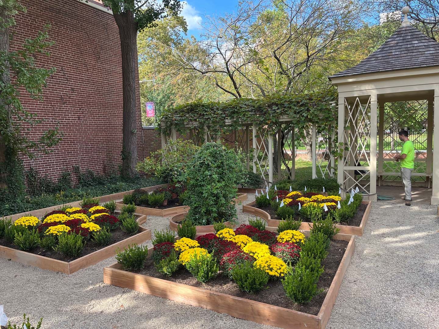 A woman is standing in a garden with flowers and a gazebo.