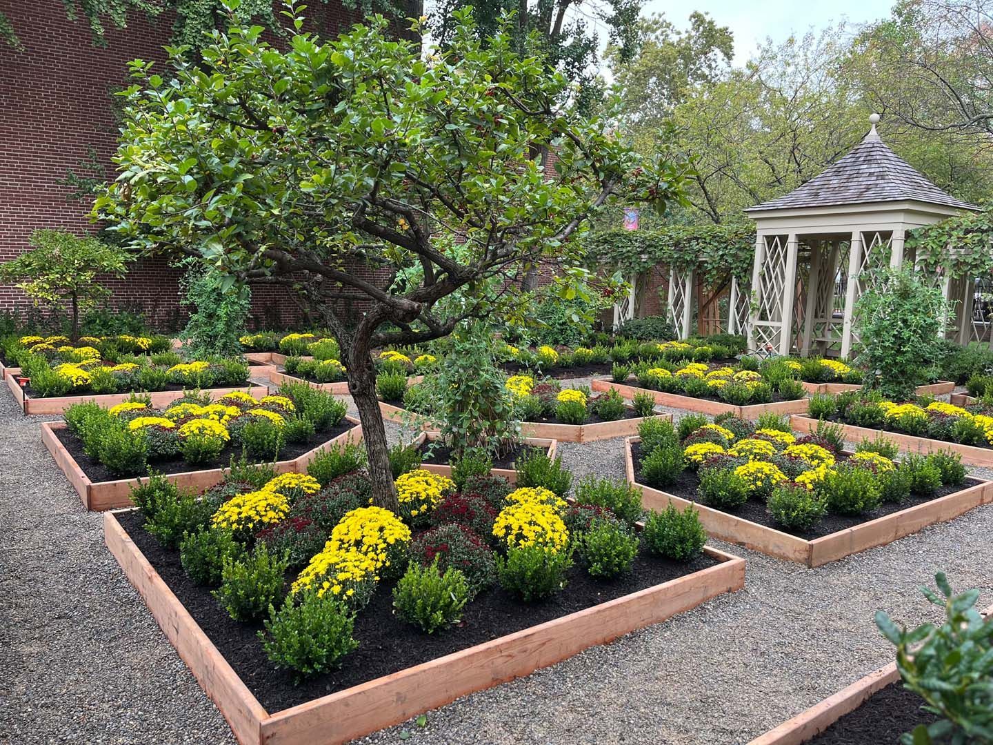 A garden with lots of flowers and trees and a gazebo in the background.